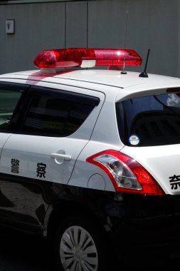 Yanıp sönen ışıkları olan bir binanın yakınına park edilmiş Japon polis arabası.