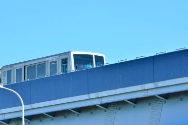 Açık mavi gökyüzüne karşı yükseltilmiş ray boyunca seyahat eden tren