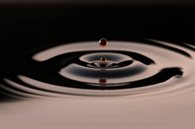 Koyu bir içecek damlası düşüyor ve daireler çiziyor.