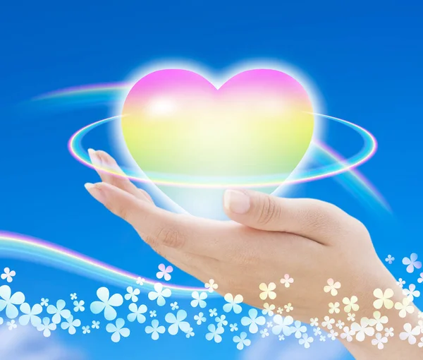 hand holding a rainbow heart with a blue sky