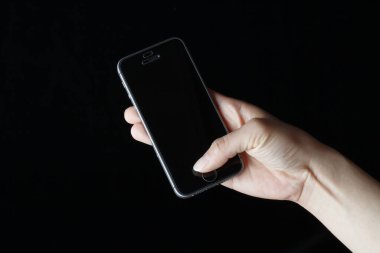 Kadın eli, siyah arkaplanda akıllı telefonu tutuyor. 