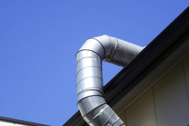 Çatıda mavi gökyüzüne karşı kıvrılan parlak metal havalandırma kanalı.