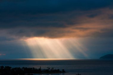 Güneşin ışınları denizin üzerindeki bulutlarda parlıyor.