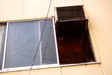 Binanın dışındaki paslı havalandırma ünitesinin yanındaki kırık cam pencere.