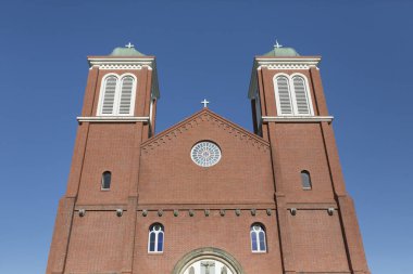 Mavi gökyüzüne karşı ikiz kuleleri olan uzun tuğlalı kilise binası.