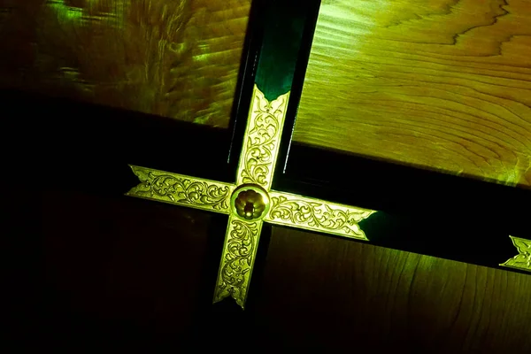 Süslü altın haç. Koyu ahşap tavan panelleri parlıyor.