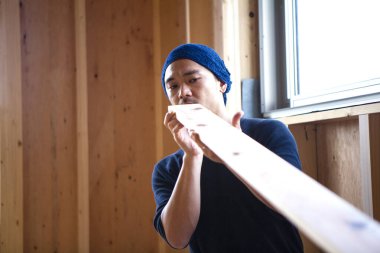 Ahşap bina inşaatında çalışan genç Asyalı marangozun portresi.