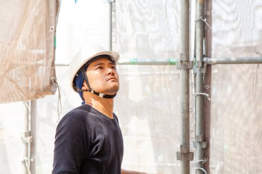 Ahşap bina inşaatında çalışan Asyalı genç bir inşaatçının portresi.