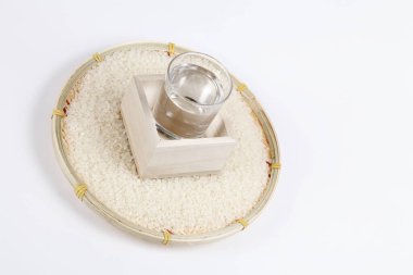 Beyaz arka planda çiğ pirinç ve bir bardak sake. Görüntüyü kapat