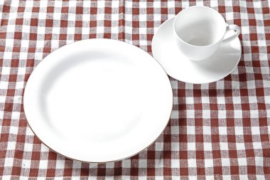 Boş beyaz tabak, kareli peçete ve çatal tahta masaya..