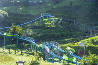 Sarmal mavi su kaydırağı yeşil çimenli yamaçtan geçiyor