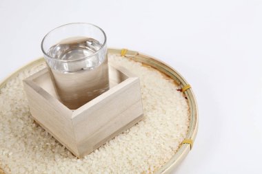 Beyaz arka planda çiğ pirinç ve bir bardak sake. Görüntüyü kapat