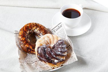 Tatlı çörekler ve beyaz masa örtüsünün üzerinde bir fincan kahve.                    