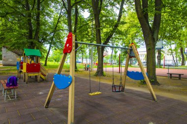 Renkli çocuk parkı salıncakları Uzun ağaçların arasında duruyor