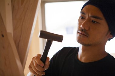 Ahşap bina inşaatında çalışan Asyalı genç bir inşaatçının portresi.