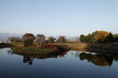 Sonbahar yaprakları ve ağaçlar sakin gölete yansıyor.