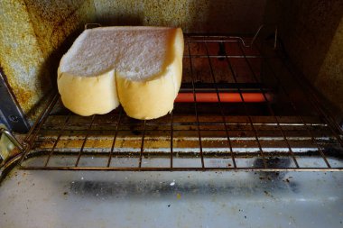 Beyaz ekmek dilimleri eski tost makinesi fırınında kızartılıyor.