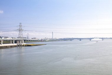 Geniş nehir berrak mavi gökyüzünün altındaki köprüleri geçiyor.