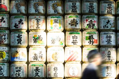 Sake fıçılarının yanından geçen bulanık bir figür.