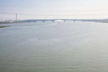 Geniş nehir açık gökyüzünün altındaki uzak köprünün altından akıyor.
