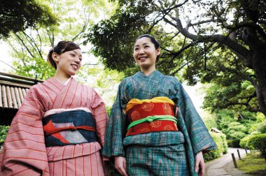 Parkta geleneksel Japon kimonosu giyen iki mutlu Asyalı kadın.
