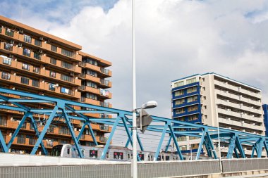 Mavi metal köprü iki uzun apartmanın arasından geçiyor.