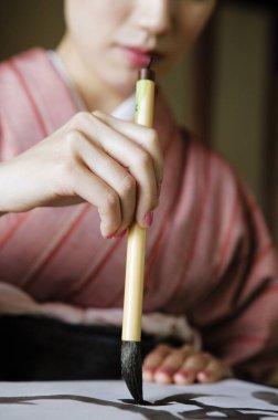 Geleneksel Japon kimonosuyla boyalı fırça ve mürekkeple yazılmış Asyalı genç bir kadının portresi. Japonca kaligrafi eğitimi  