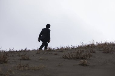 Siyah ceketli Asyalı işadamı kumda yürüyor. 