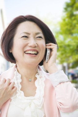 Asyalı olgun bir kadın şehirdeki akıllı telefondan arıyor.