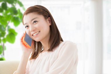 Kanepede akıllı telefonlu gülümseyen Japon kadın.