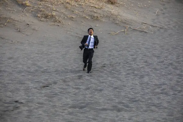 asian businessman in formal suit running along the sandy beach