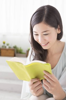 Evde kitap okuyan Asyalı kadın.