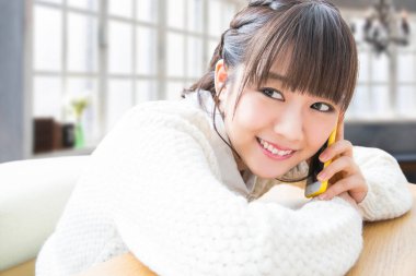 Genç Asyalı kadın akıllı telefonda konuşurken gülümsüyor. 