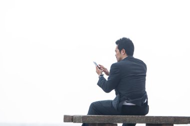 Genç Asyalı işadamı cep telefonunu bankta, dikiz aynasından kullanıyor. 