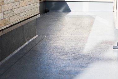 Taş duvarın yanındaki ışığı yansıtan pürüzsüz gri yüzey