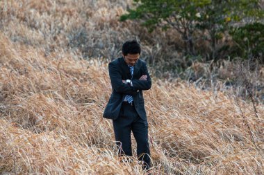 Genç Asyalı işadamı tarlada çapraz kollarla yürüyor. 