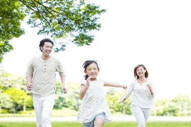 Küçük kızıyla birlikte yaz parkında koşan mutlu Asyalı ebeveynlerin portresi.