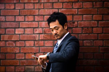 Şehirdeki tuğla duvarın yanında cep telefonu kullanan Asyalı işadamı 