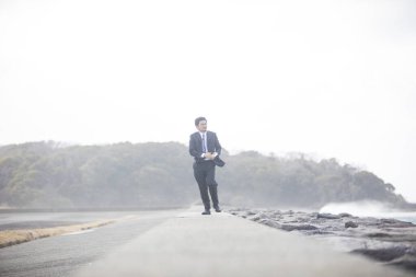 Siyah takım elbiseli Asyalı işadamı deniz kıyısında yürüyor. 