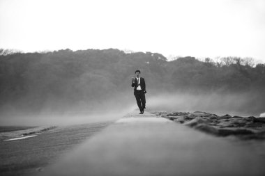 Siyah takım elbiseli Asyalı işadamı deniz kıyısında yürüyor. 