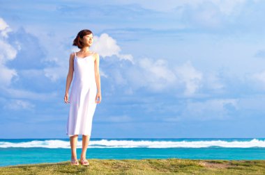 Beyaz elbiseli kadın tropikal sahilde yürüyor.