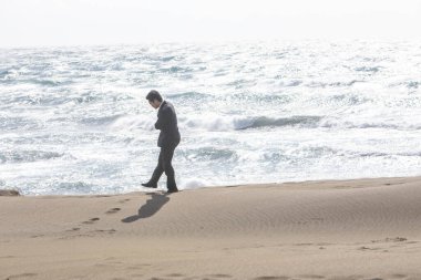 Siyah takım elbiseli genç Asyalı işadamı sahilde yürüyor.