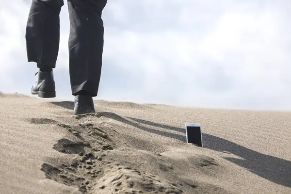 low section of businessman walking through phone which is stuck in sand