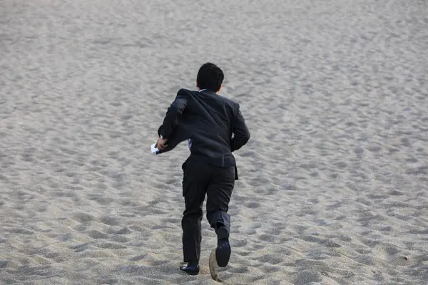 asian businessman in formal suit running along the sandy beach, back view