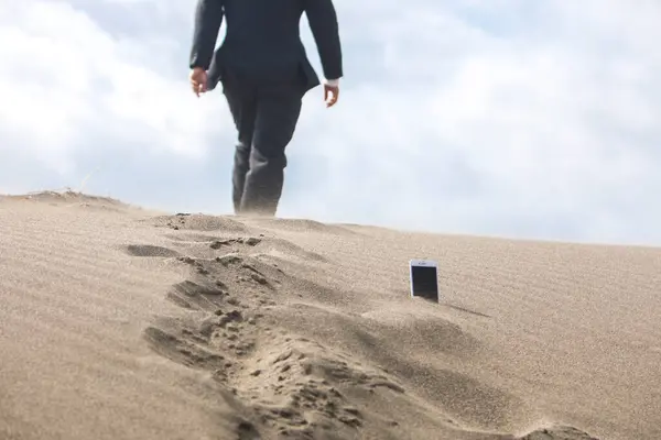 low section of businessman walking through phone which is stuck in sand