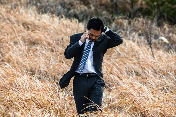 asian businessman in formal suit talking on phone in a field