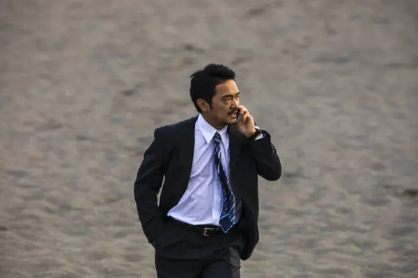 asian businessman in formal suit talking on phone while walking along the sandy beach