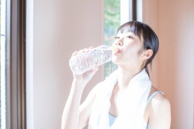 Spor salonundaki antrenmandan sonra su içen Asyalı kadın.