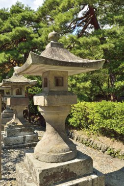 Yeşil ağaçların ve çalıların arasında duran taş fenerler.