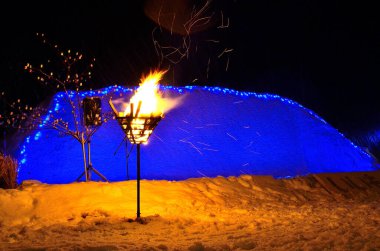 Yanan meşale, parlayan mavi eskimo evinin yanında karlı zemin aydınlatıyor.